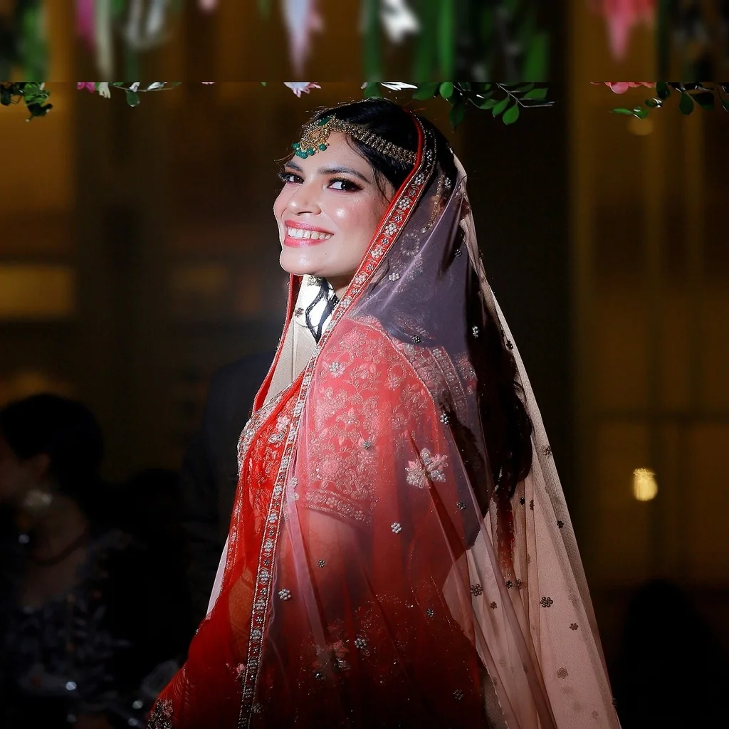 Radiant smiling bride looking over shoulder in red veil by Wedding Shedding