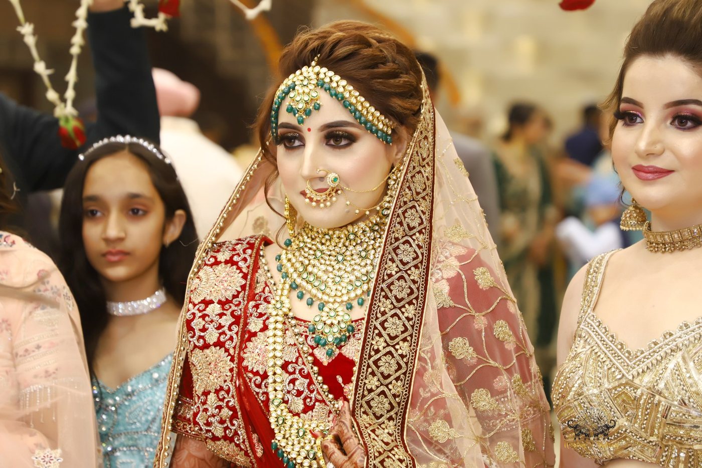 Bride in royal red lehenga entering under floral chandelier