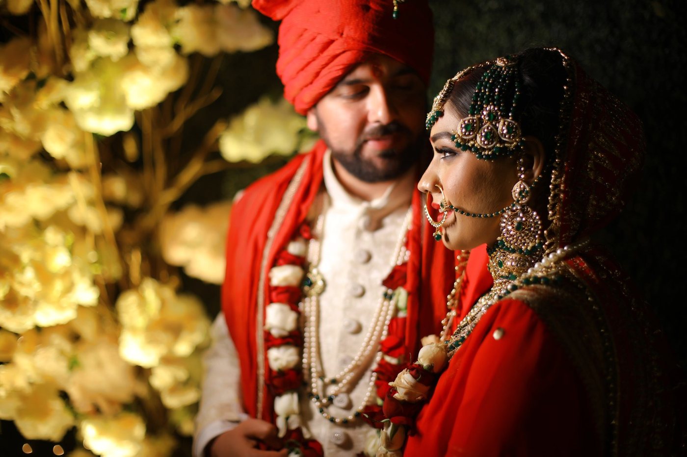 Bride and groom in red turban and lehenga with warm golden bokeh